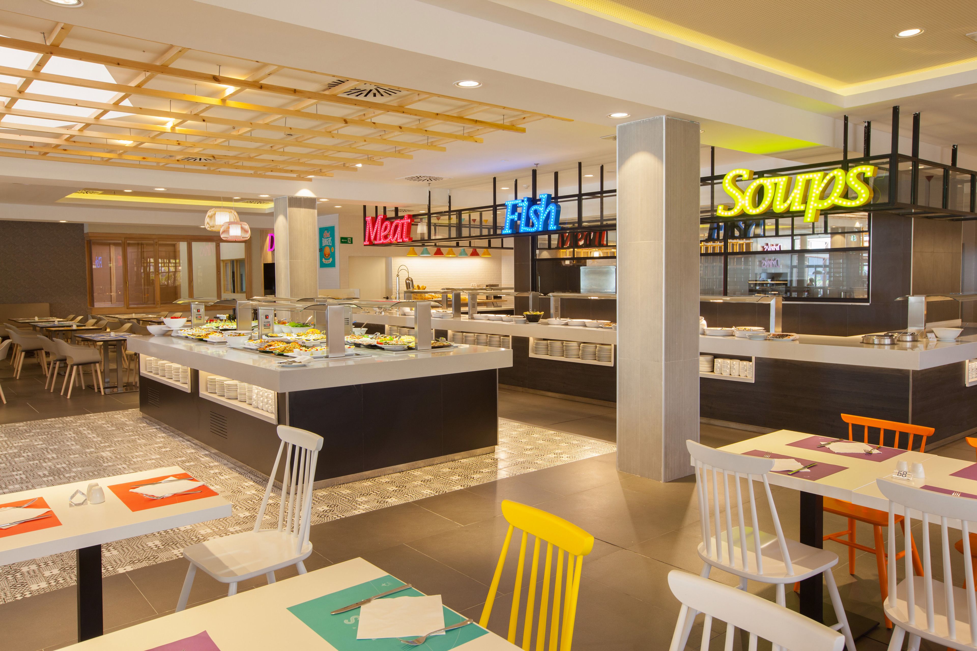 Un restaurante moderno con una isla central, varias zonas de estar y señalización clara para las distintas secciones de comida.