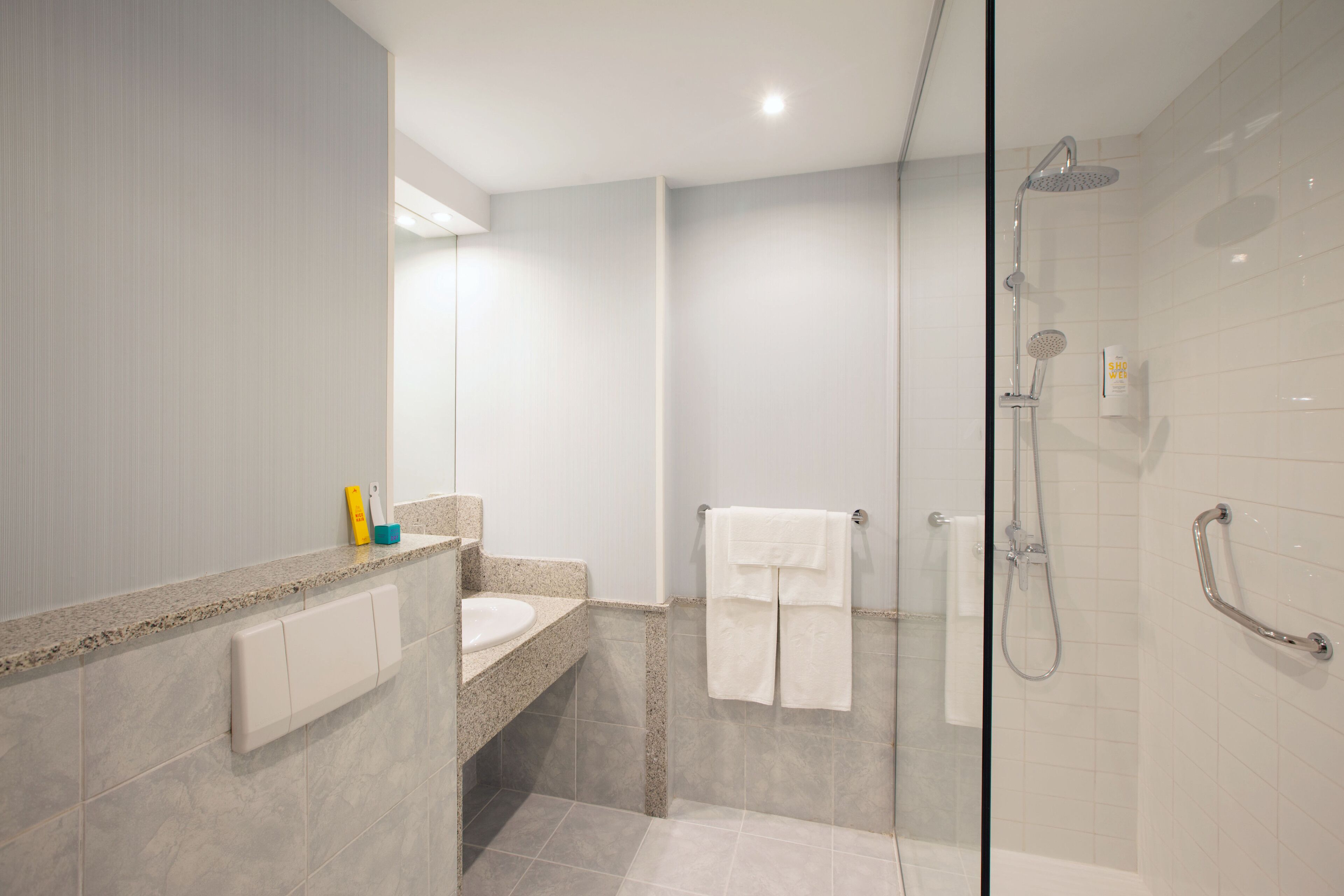 A modern bathroom with a glass shower enclosure, a granite countertop, and a white sink.