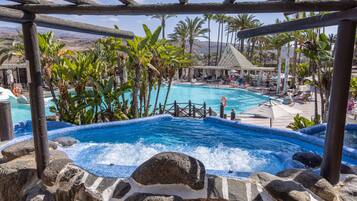 Relax by the pool surrounded by lush tropical plants and natural rock formations, with a hot tub and lounge chairs available.