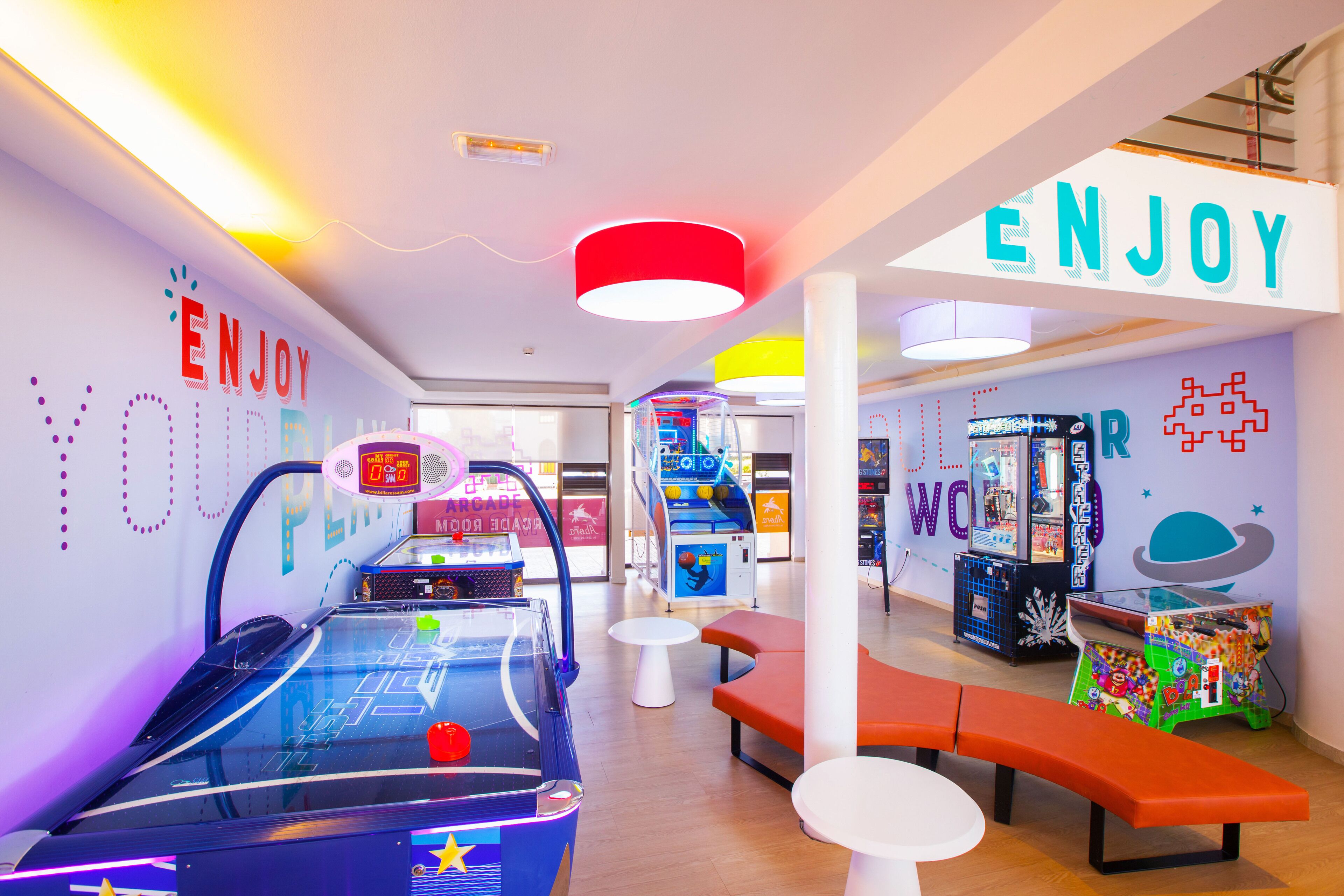 Un salón de juegos muy iluminado con letreros de neón y diversas máquinas recreativas.