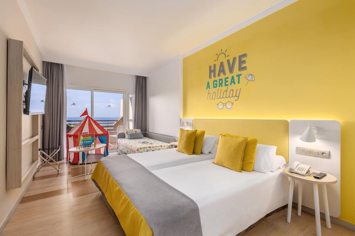 A hotel room with two beds, a play tent, a large window with a view, and a motivational wall quote.
