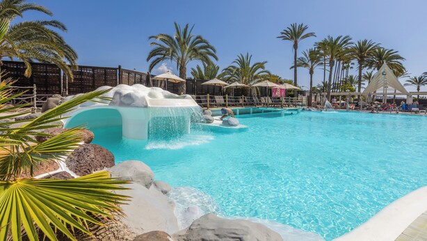 A pool with a waterfall feature, surrounded by palm trees and umbrellas. - Abora Continental by Lopesan Hotels - All Inclusive (San Bartolomé de Tirajana)
