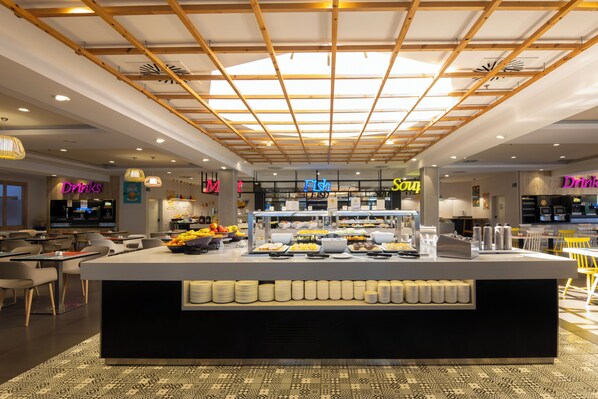 A modern cafe with a central counter displaying food and drinks, surrounded by seating areas.