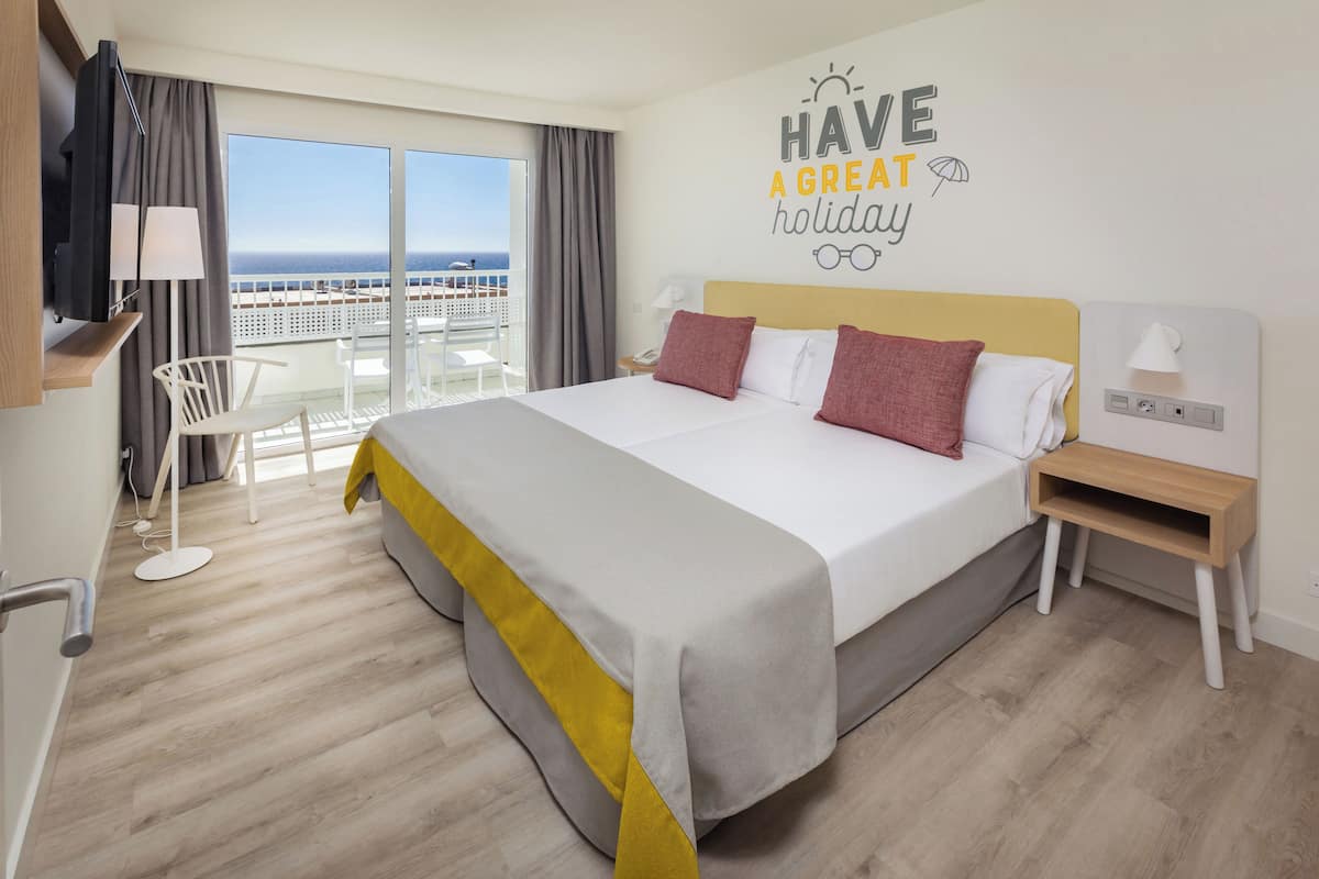 Une chambre d’hôtel avec un grand lit, un balcon avec vue, un bureau et une chaise.