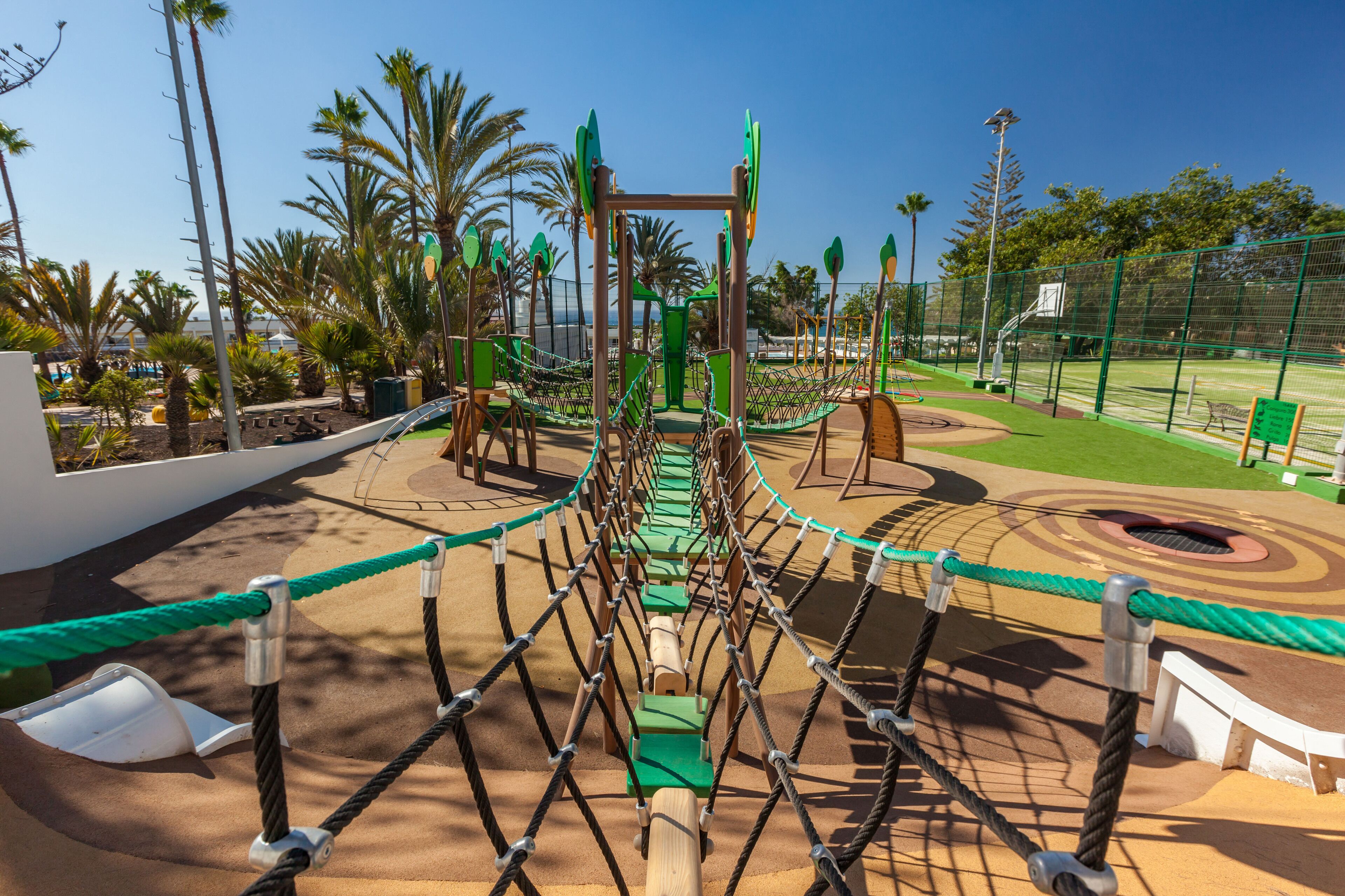 Ein Spielplatz mit einer Seilbrücke, Palmen und einem Basketballplatz.