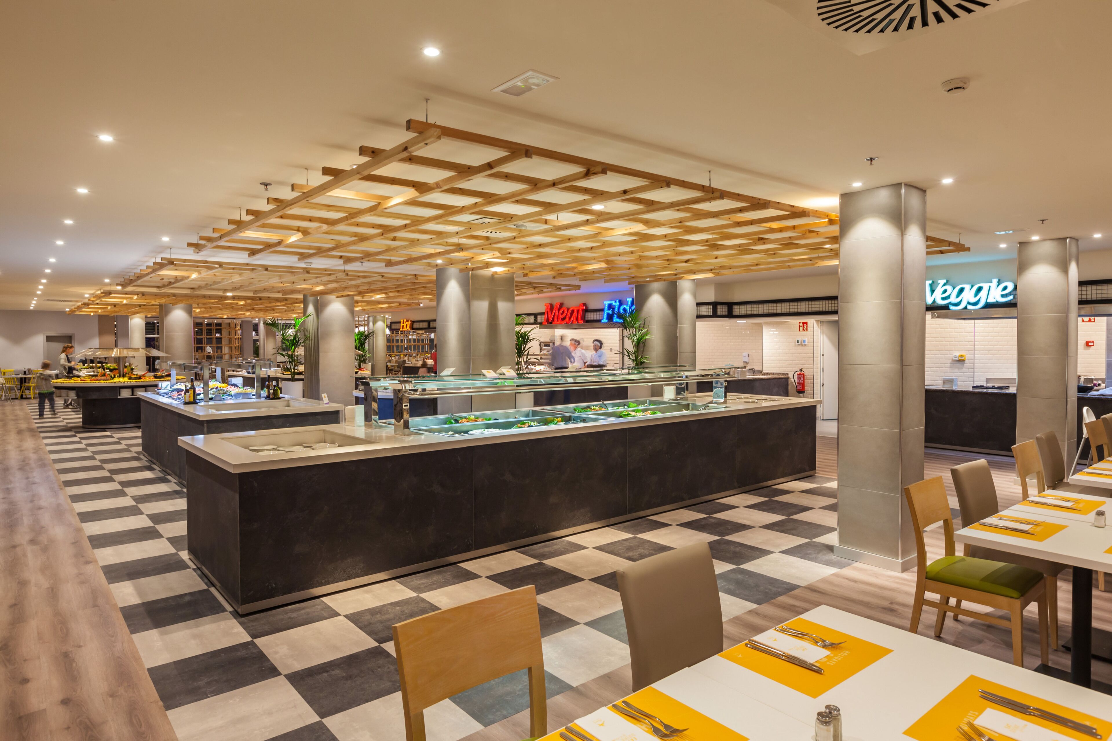 Un restaurante moderno con suelo de cuadros, un bufé central y un letrero que dice 'Veggie'.