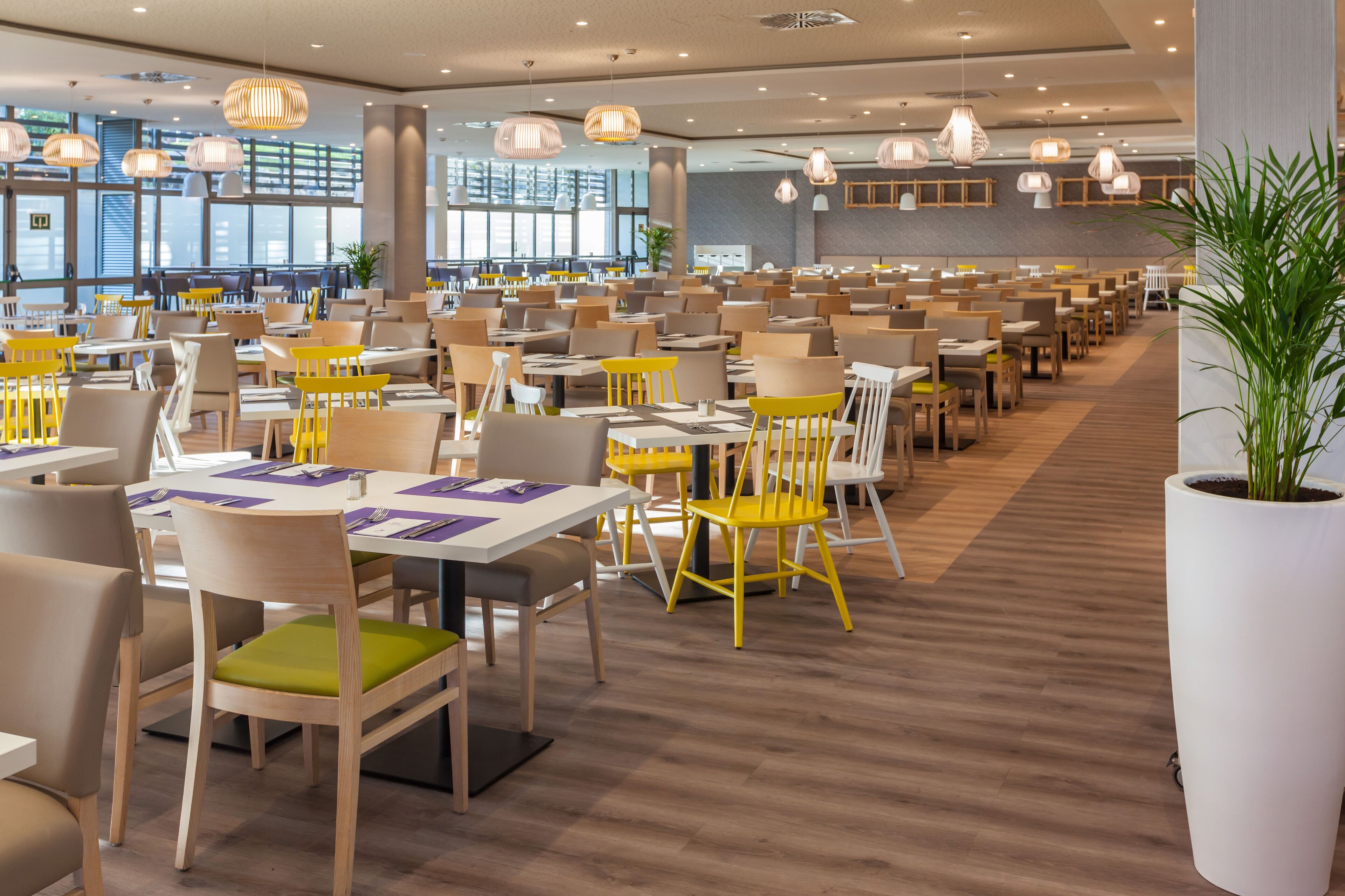 Un comedor espacioso con varias mesas y sillas, ventanas amplias y lámparas colgantes.