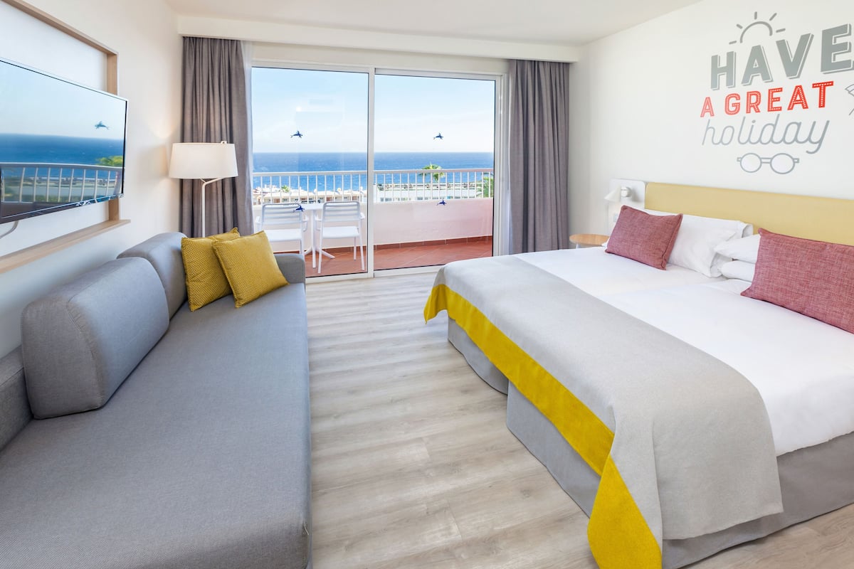 Une chambre d’hôtel avec un balcon, un lit, un canapé et une télévision.