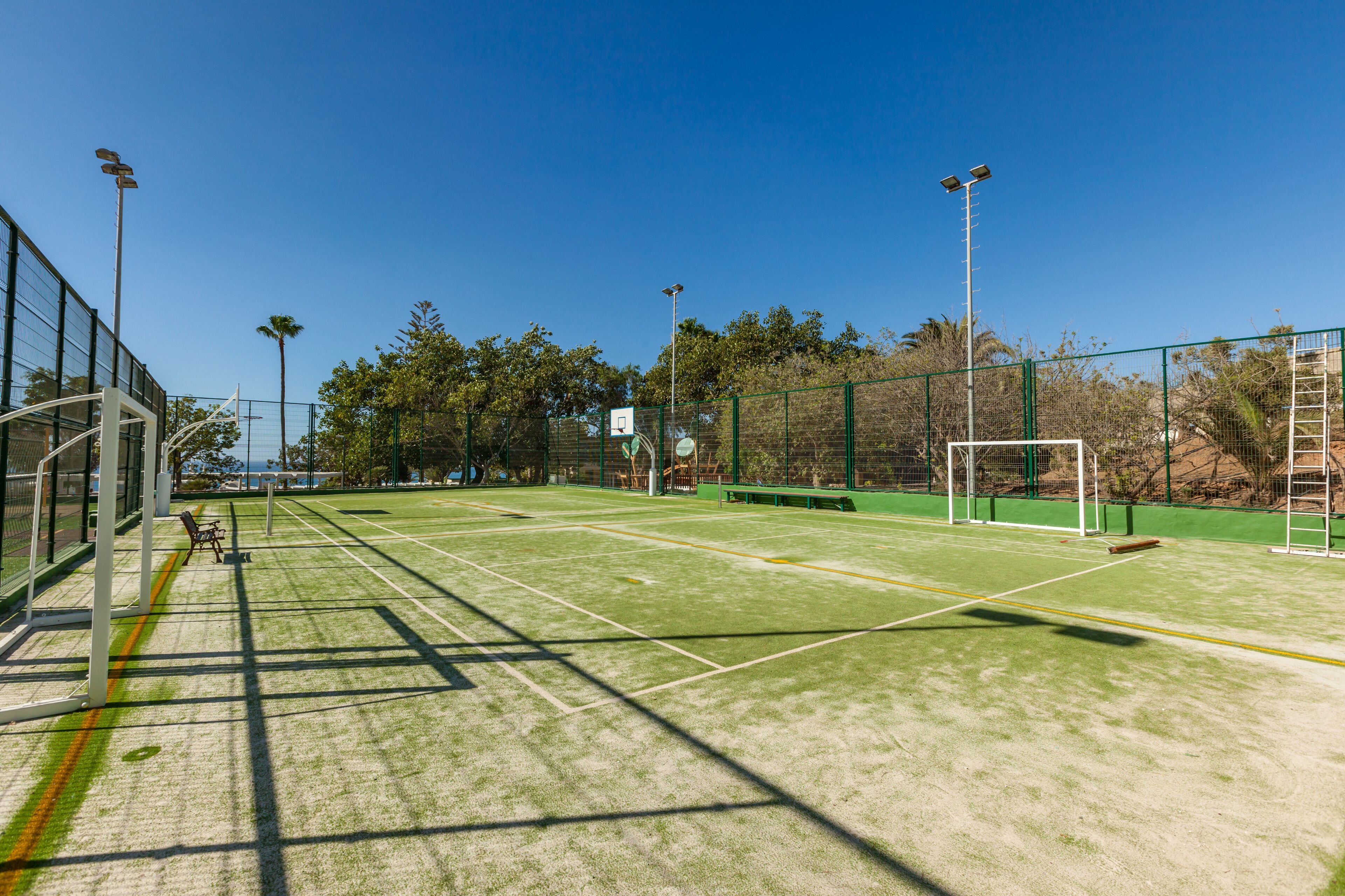 An outdoor tennis court with green artificial turf, goalposts, and solar-powered floodlights.