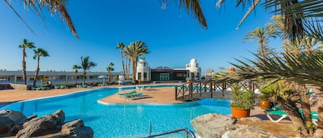 A swimming pool with a clear blue water, surrounded by palm trees and lounge chairs.
