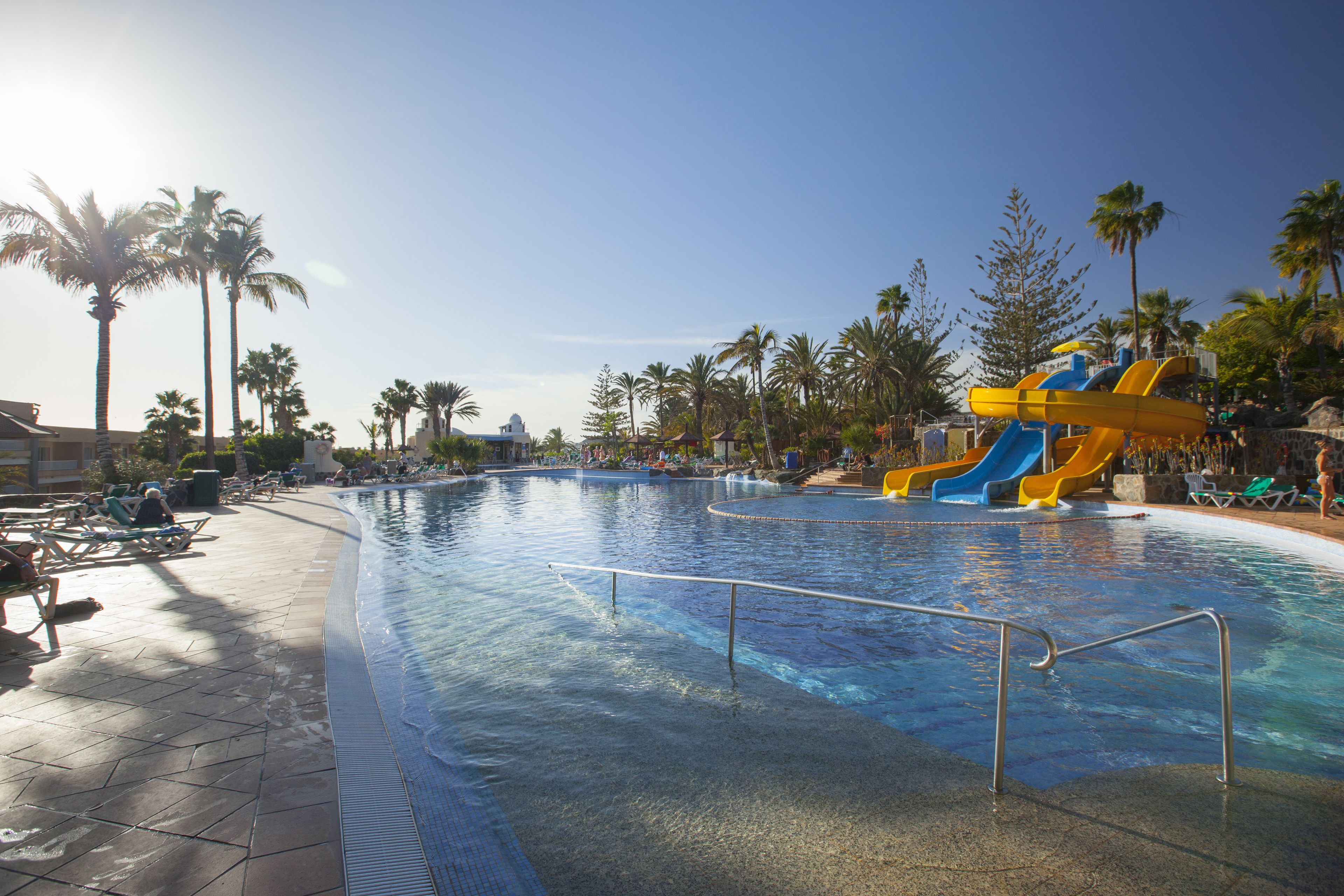 A swimming pool with a water slide, palm trees, and lounge chairs.