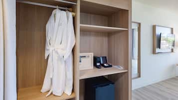 A hotel room with a wooden wardrobe, a robe hanging inside, a small desk with a phone and a coffee machine, and a TV mounted on the wall.