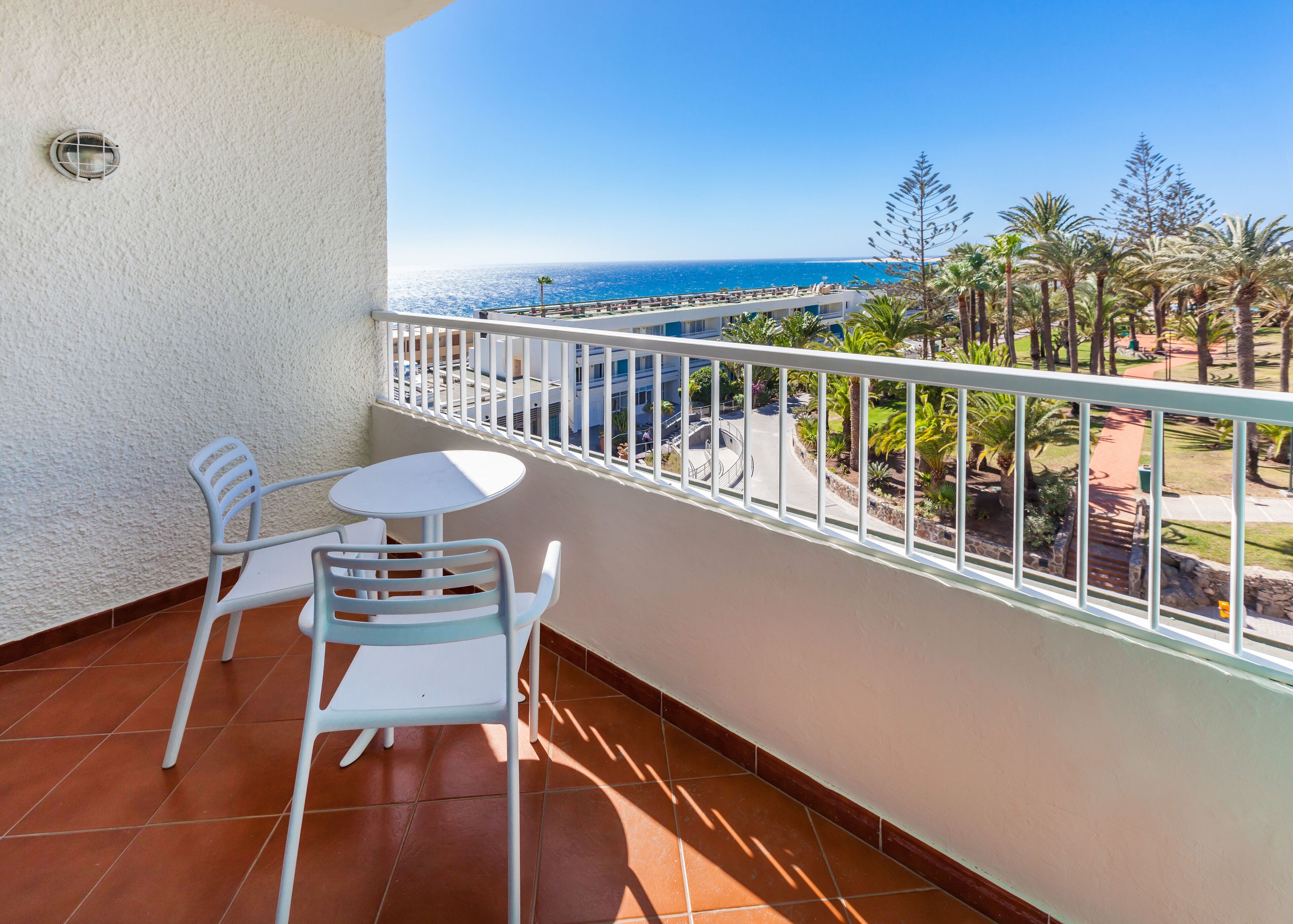 A balcony with a white railing, a small round table, and two white chairs.