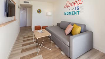 Una sala de estar moderna con un sofá gris, suelo de madera, una mesita y un televisor montado en la pared.