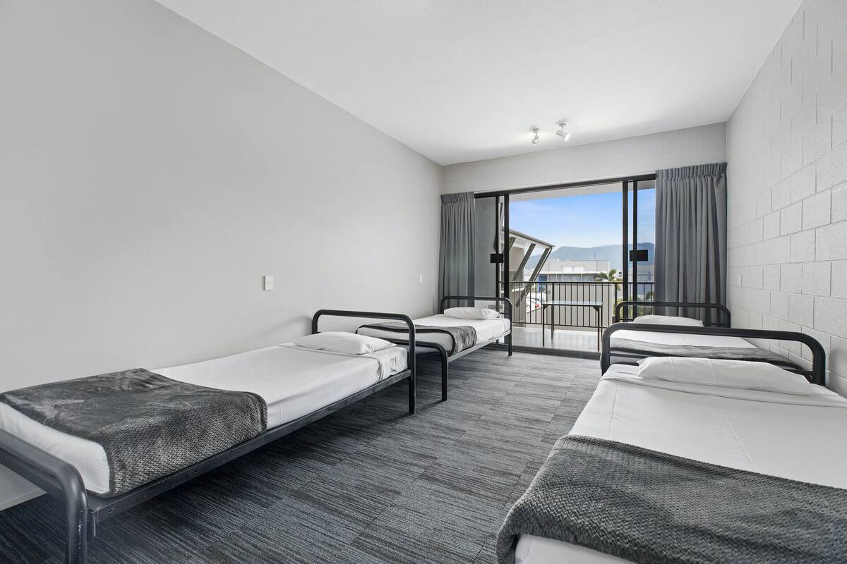 A hotel room with three single beds, a balcony with a view, and a sliding door to the outside.
