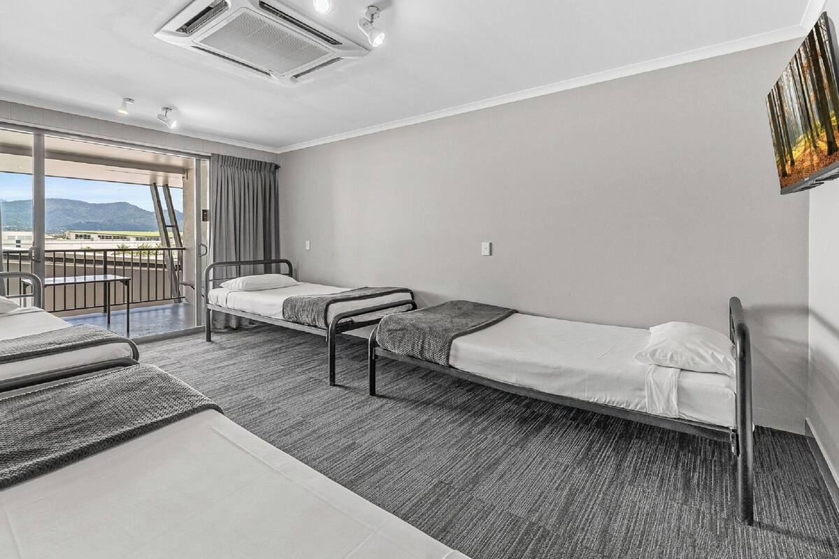 A hotel room with two single beds, a large window with a view of mountains, and a balcony with a railing.