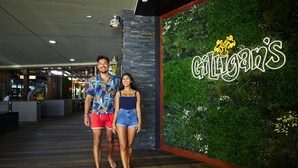 A couple standing in front of a restaurant named "Gili's" with a green wall and a neon sign.