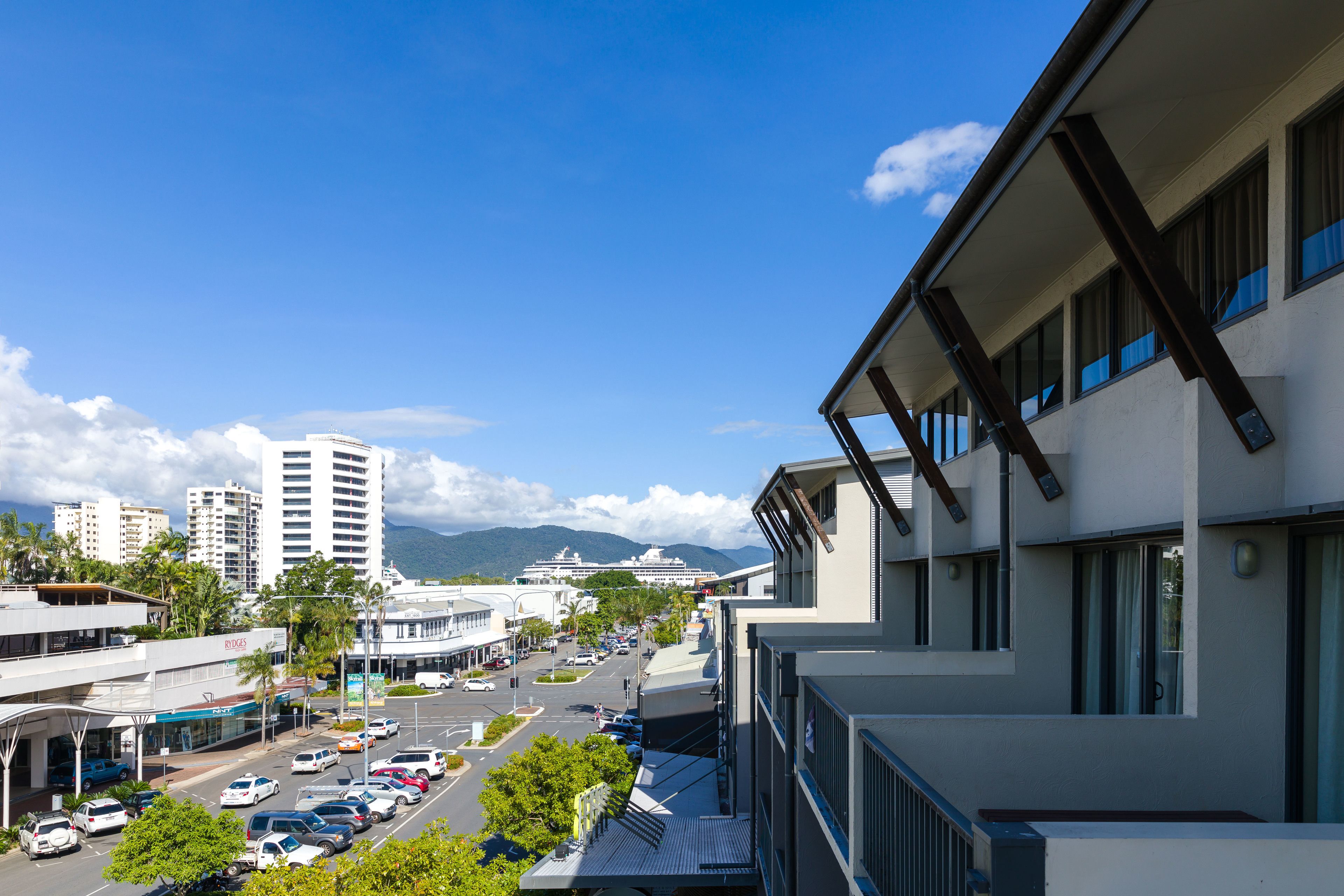 A modern building with large windows and a view of a busy street and mountains in the background.