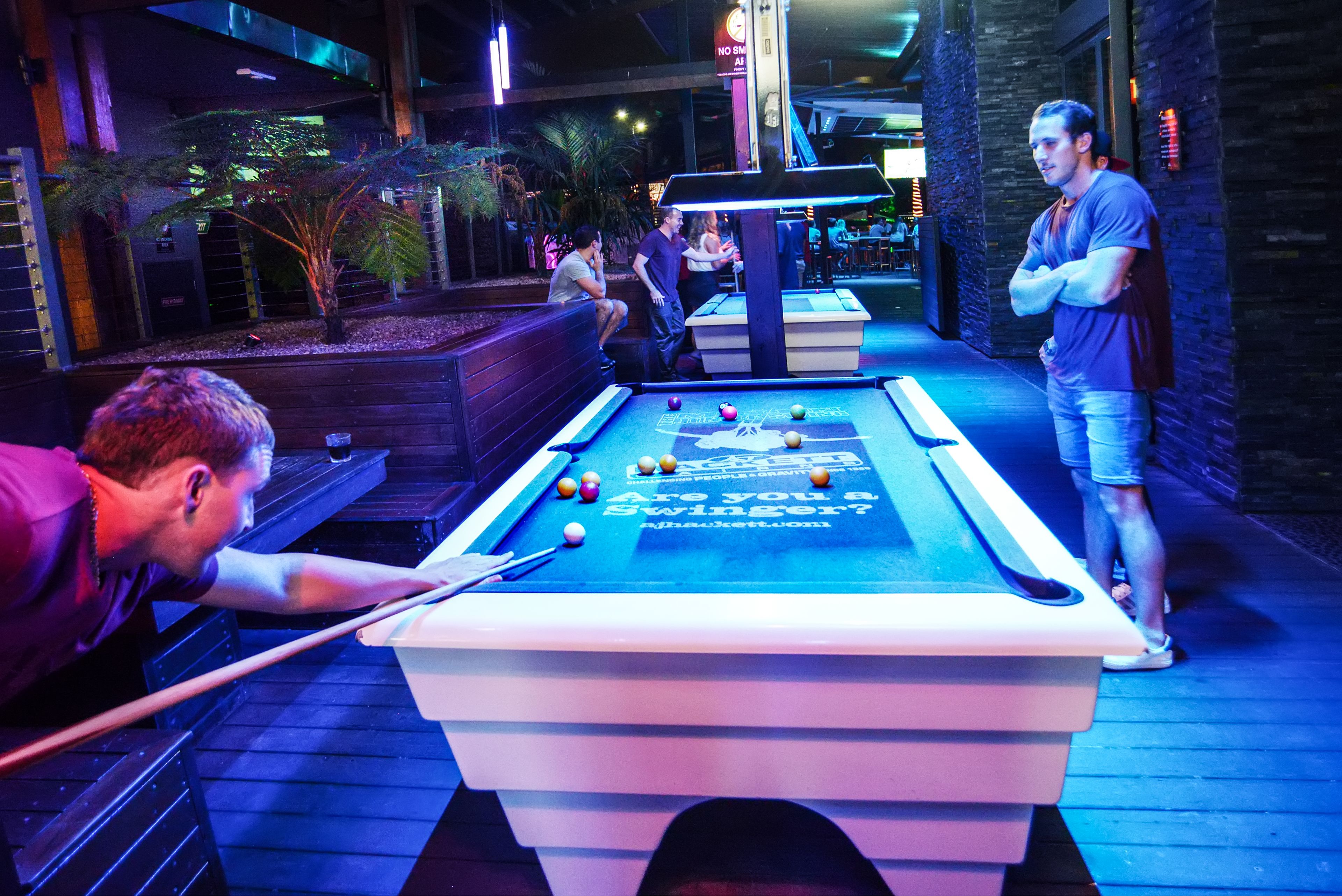 A pool table with a game in progress, surrounded by a wooden deck and a seating area.