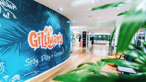A Gili's restaurant with a tropical theme, featuring a curved wall with the restaurant's logo and the tagline "Stay, Play + Explore".