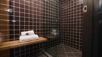 Une salle de bain moderne avec des murs recouverts de carreaux foncés, une douche en verre et une étagère en bois sur laquelle sont posés une serviette et des articles de toilette.