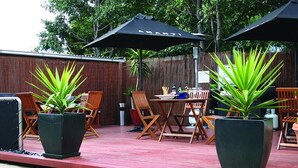 An outdoor patio area with wooden chairs and tables, large potted plants, and umbrellas. - Birches Serviced Apartments (East Melbourne)