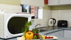A kitchen with a microwave, sink, kettle, toaster, and a plate of vegetables. - Birches Serviced Apartments (East Melbourne)