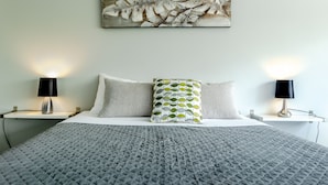 A neatly made bed with a patterned pillow, a wall-mounted artwork, and bedside lamps. - Birches Serviced Apartments (East Melbourne)