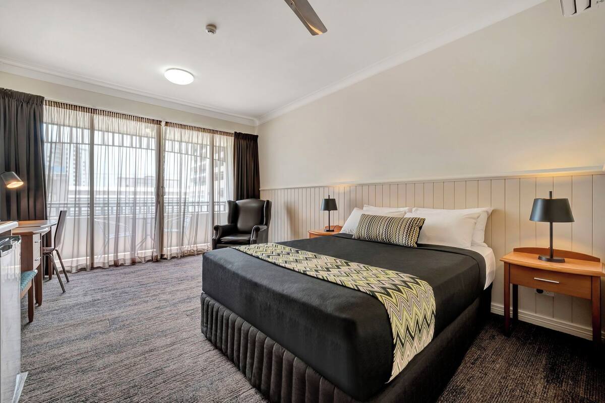 Une chambre d’hôtel avec un grand lit, un bureau, une chaise et une fenêtre avec des rideaux.