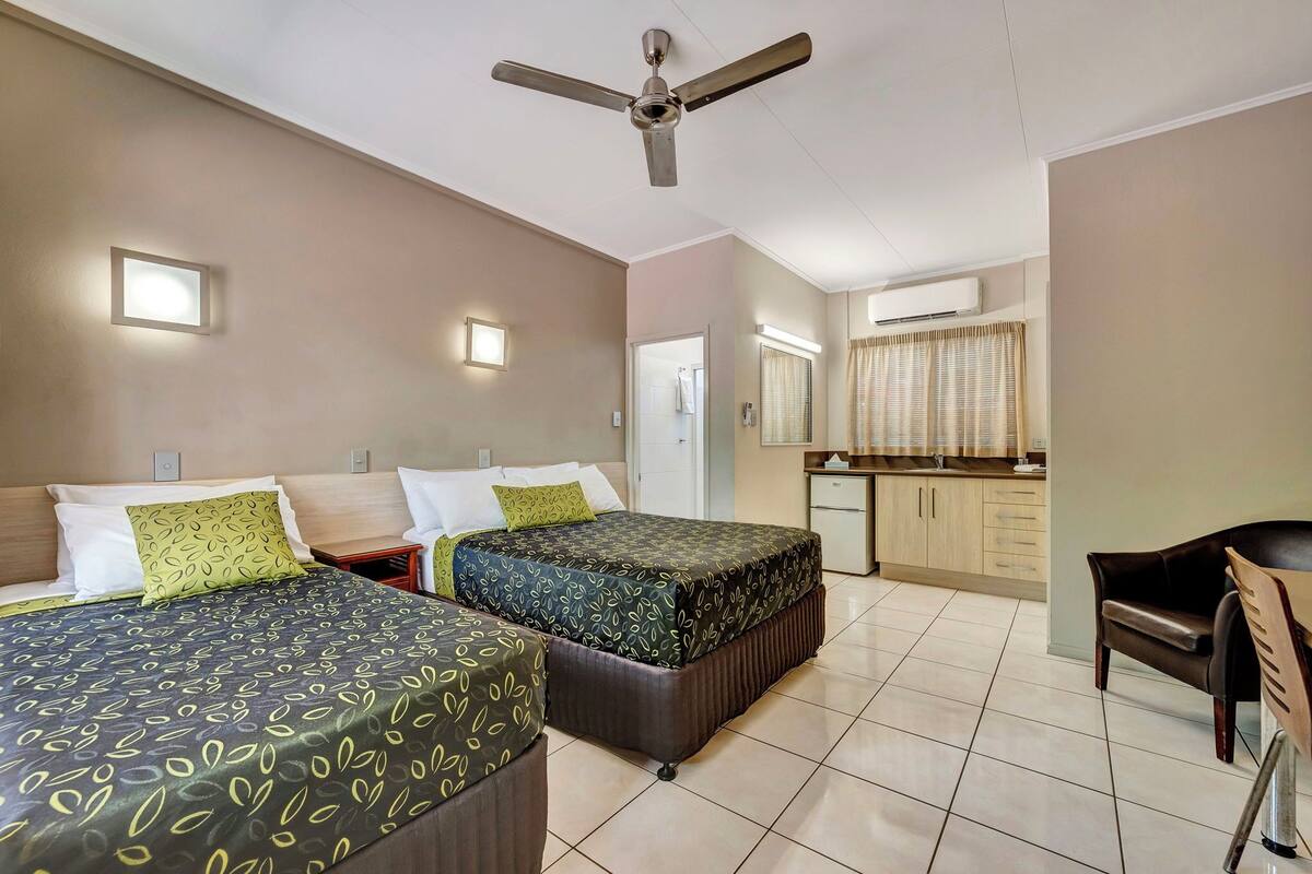 Une chambre d’hôtel avec deux lits, un ventilateur de plafond, un petit coin cuisine et un espace repas.