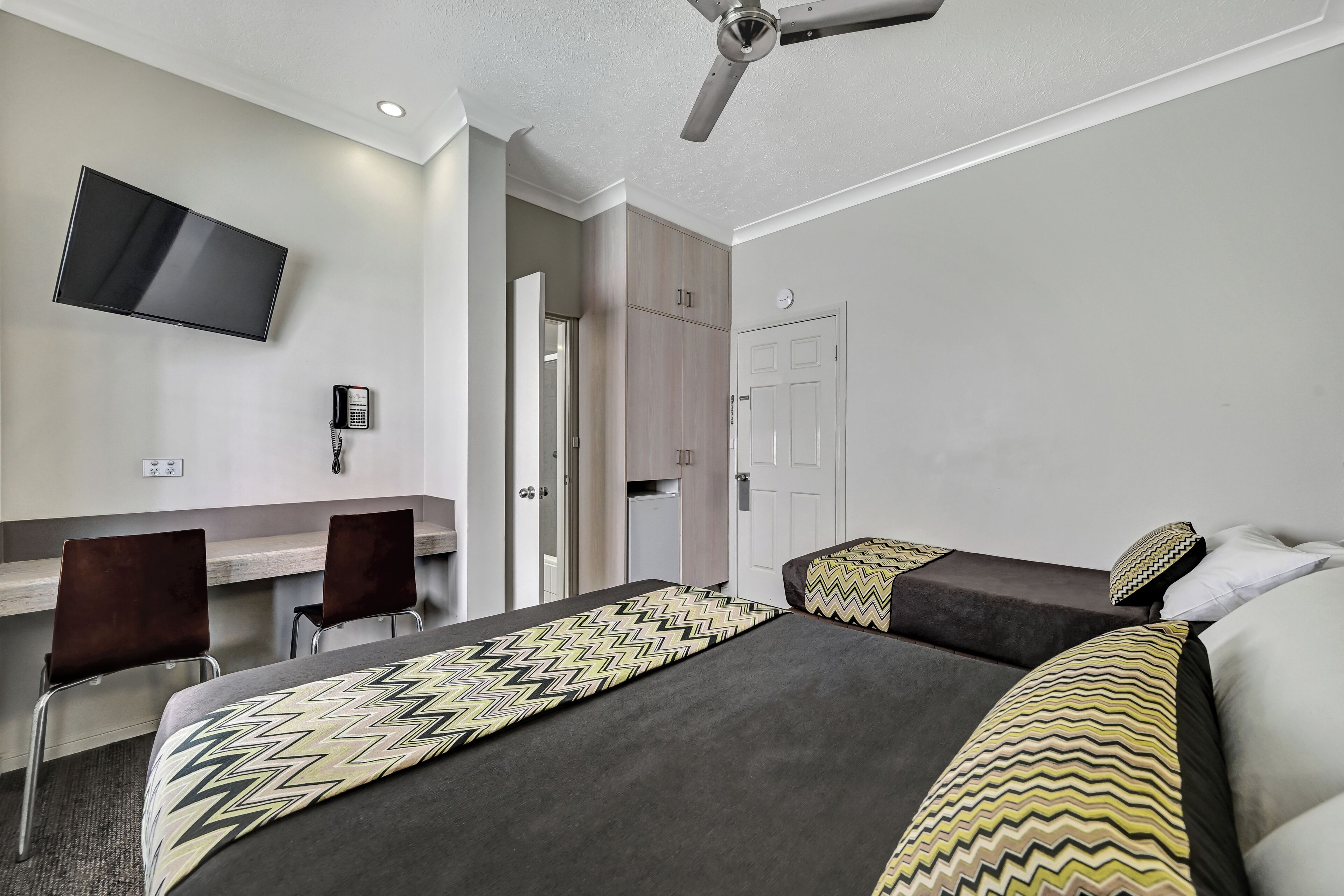 Habitación de hotel con dos camas, un escritorio, una silla, un televisor y un ventilador de techo.