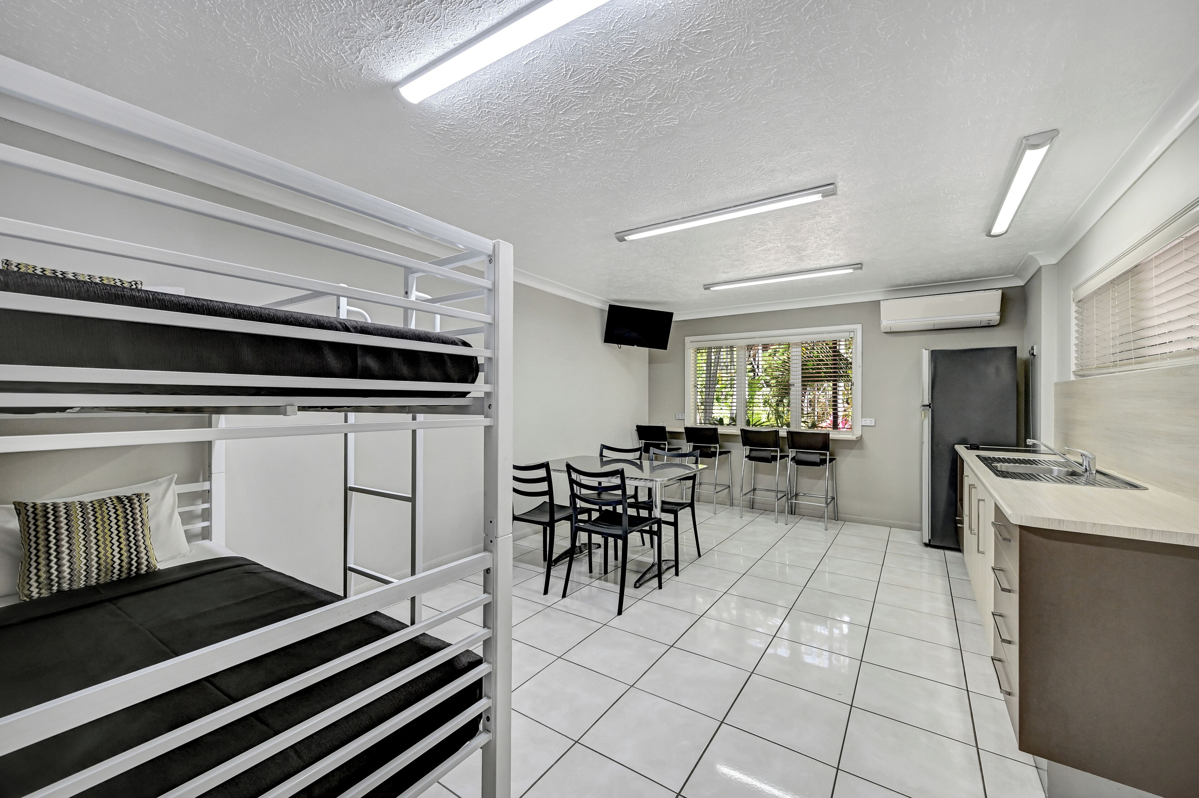 A modern, well-lit room with bunk beds, a kitchen area with a sink and stove, and a dining table with chairs.