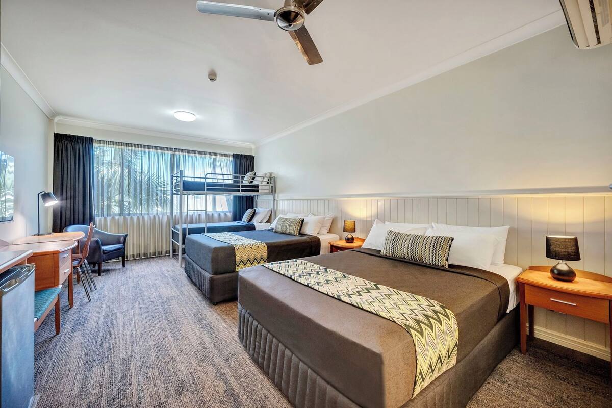 Une chambre d’hôtel avec deux lits, un bureau, une chaise, une lampe et un ventilateur de plafond.