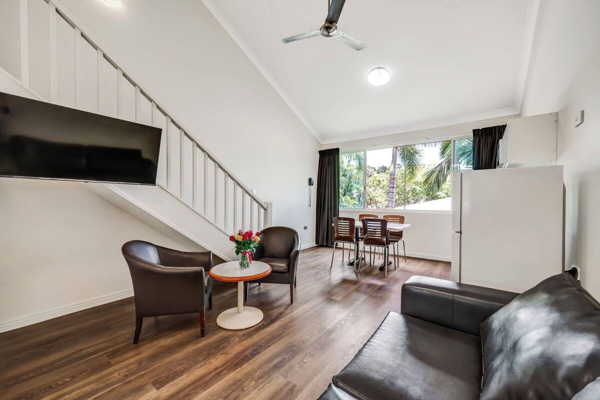 Un salon moderne doté d’un téléviseur à écran plat, d’un canapé, d’un coin repas avec des chaises, d’un escalier et d’un ventilateur de plafond.