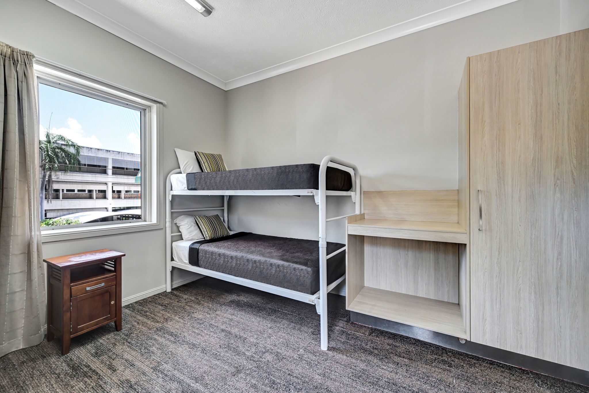 Ein Schlafraum mit Etagenbett, einem Fenster, einem kleinen Holzschrank und Teppichboden.