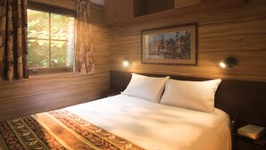A neatly made bed with white linens, a patterned rug, a painting on the wall, and a window with curtains. - Disney Davy Crockett Ranch (Bailly-Romainvilliers)