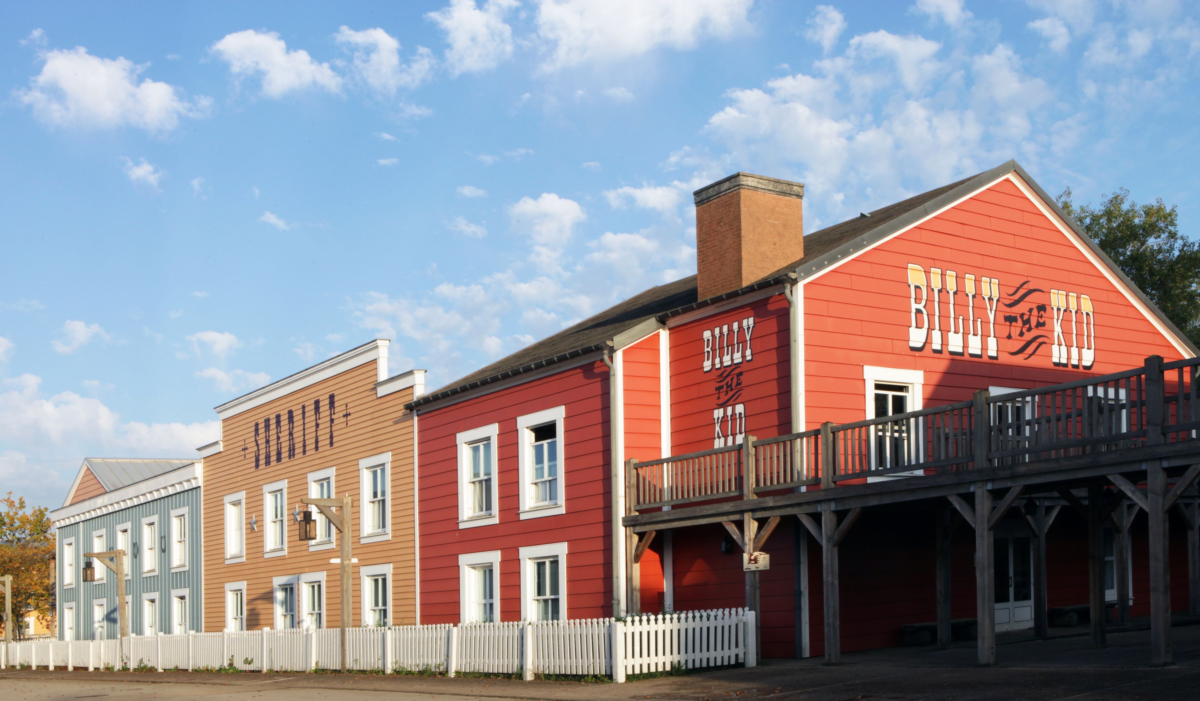 A red building with a sign reading "Billy the Kid" and a white picket fence in front.