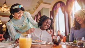 Une salle à manger avec des lustres, une table garnie de plats et de boissons, et une personne en robe.
