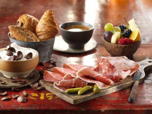 A charcuterie board with various meats, pickles, and bread, accompanied by a bowl of chocolate and a cup of coffee. - Disney Hotel Santa Fe (Coupvray)