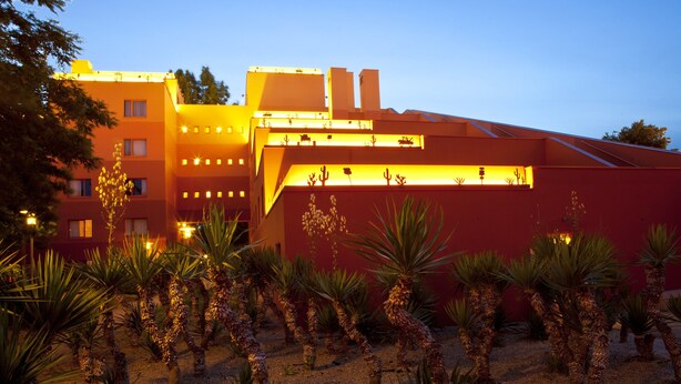 A building with multiple floors, a red facade, and a garden with palm trees. - Disney Hotel Santa Fe (Coupvray)