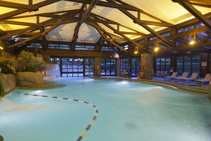 An indoor swimming pool with a waterfall feature, wooden beams, and lounge chairs. - Disney Sequoia Lodge (Coupvray)