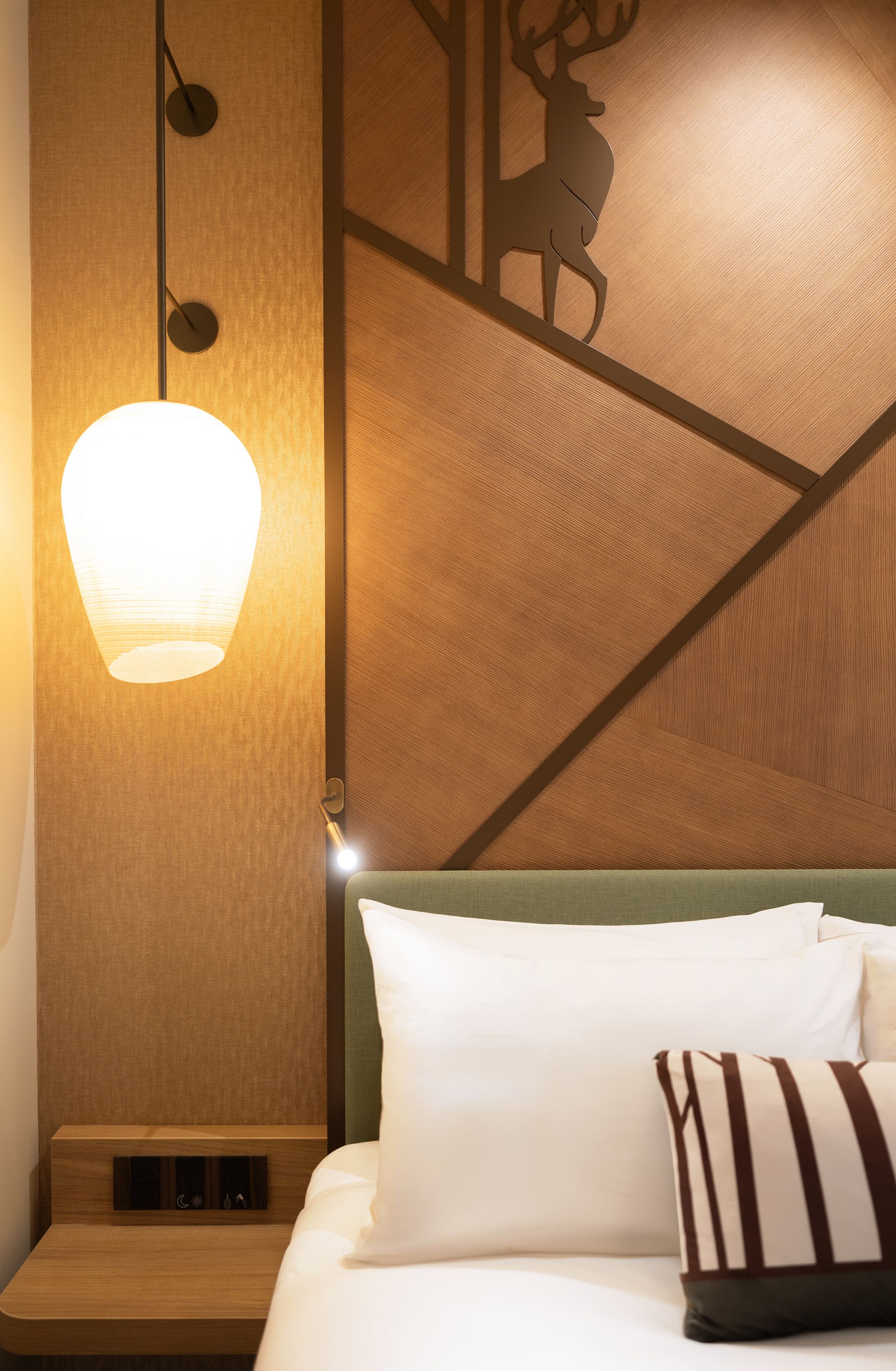 Een hotelkamer met een houten hoofdbord, een wandklok, een bed met witte lakens en een decoratief wandpaneel.