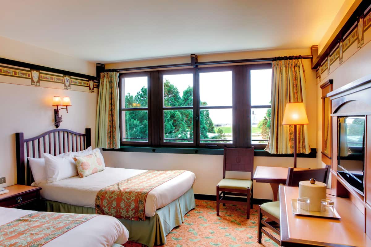 Una habitación de hotel con cama, una silla, una mesa con lámpara y una televisión.