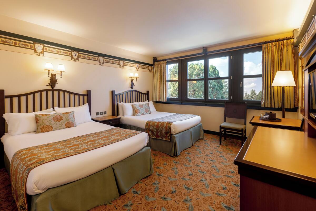 A hotel room with two beds, a desk, and a chair.