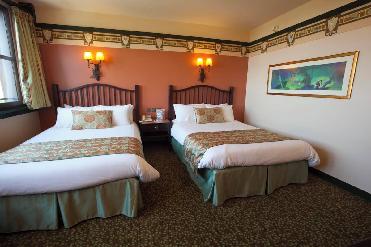 Habitación de hotel con dos camas, cada una con colcha verde y almohadas a juego, una mesita de noche con lámpara, y un cuadro en la pared.