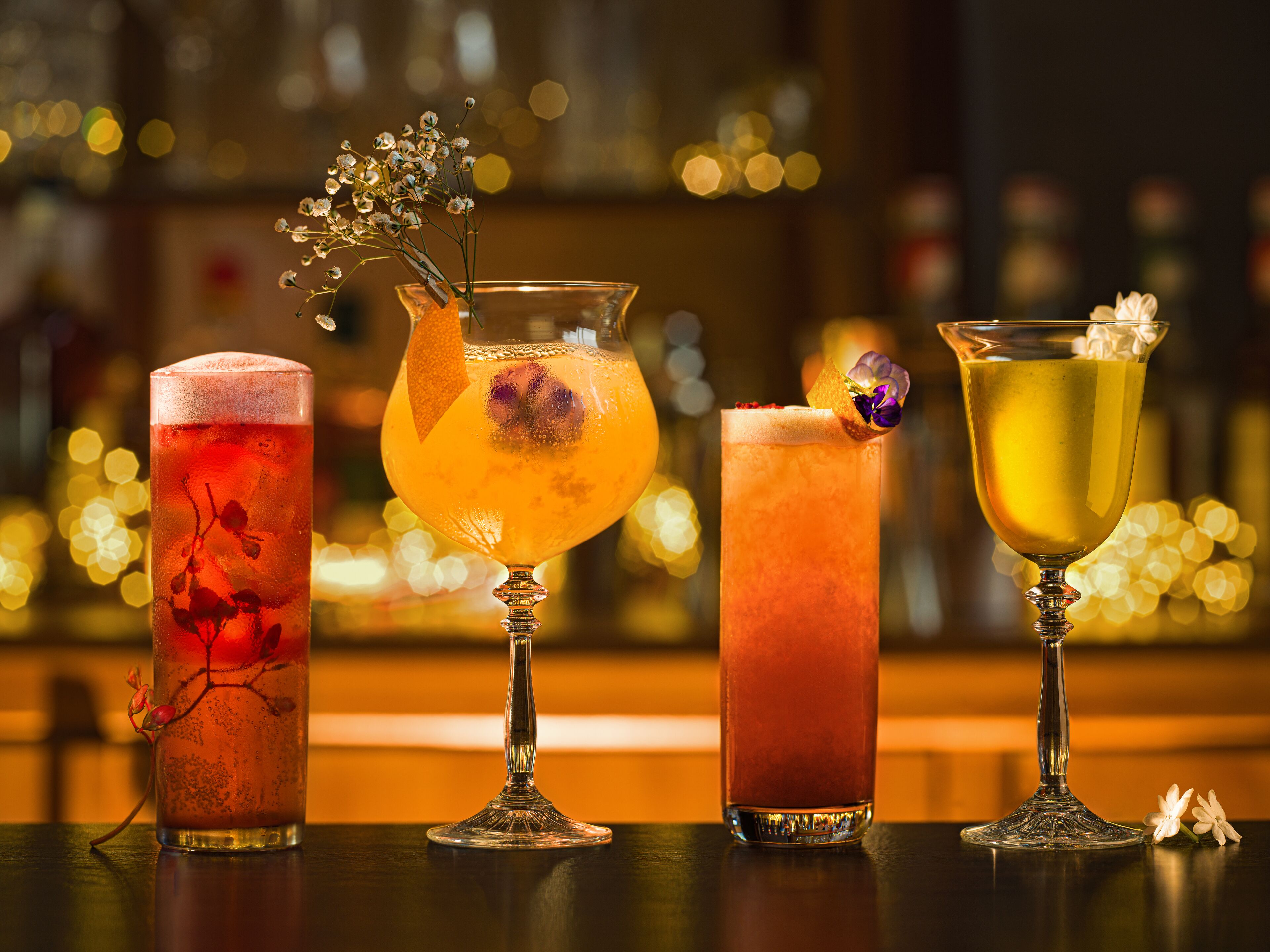 Four different cocktails in various glassware on a bar counter.