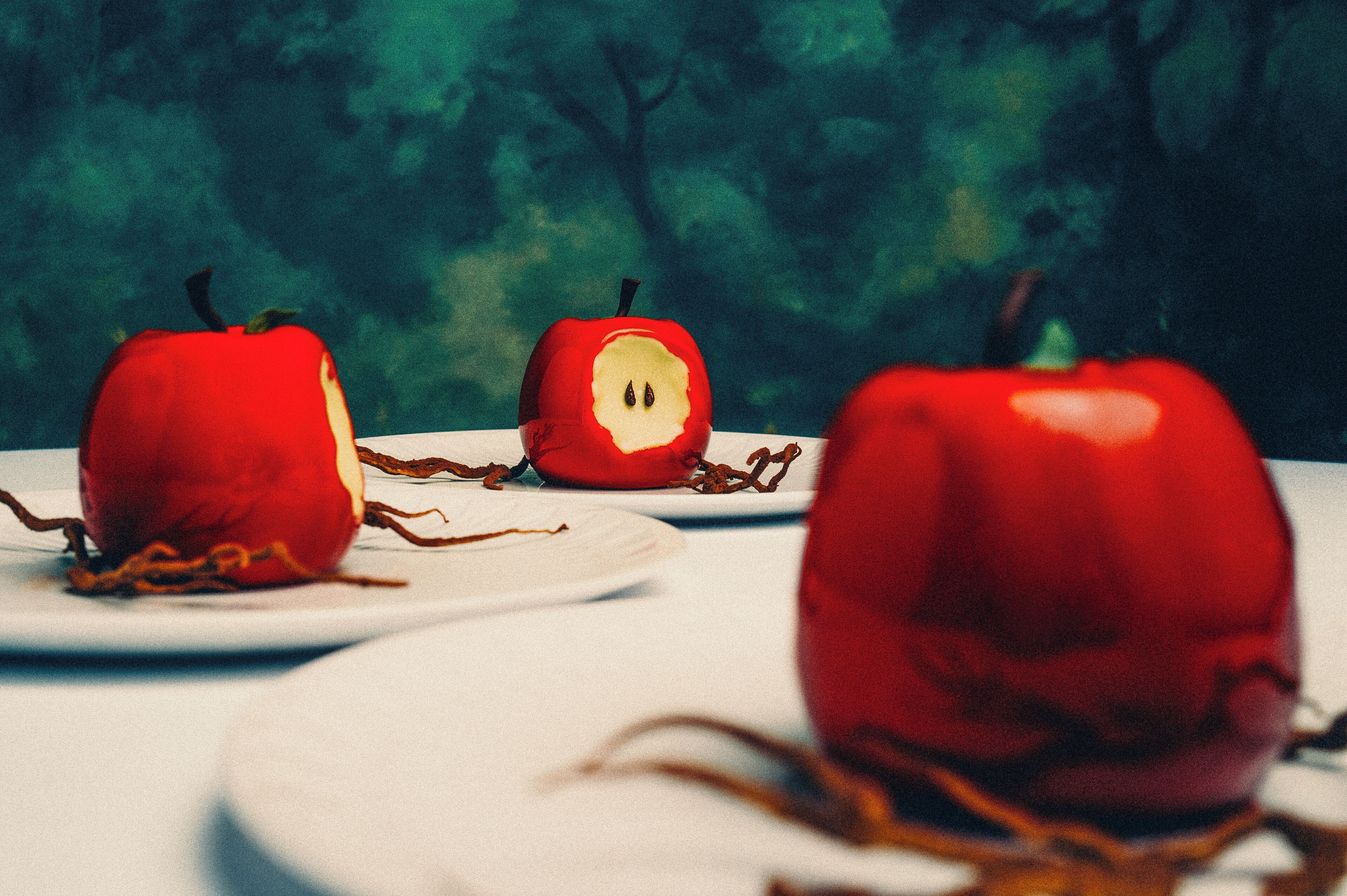Trois pommes rouges sur des assiettes blanches, avec un arrière-plan vert flou.