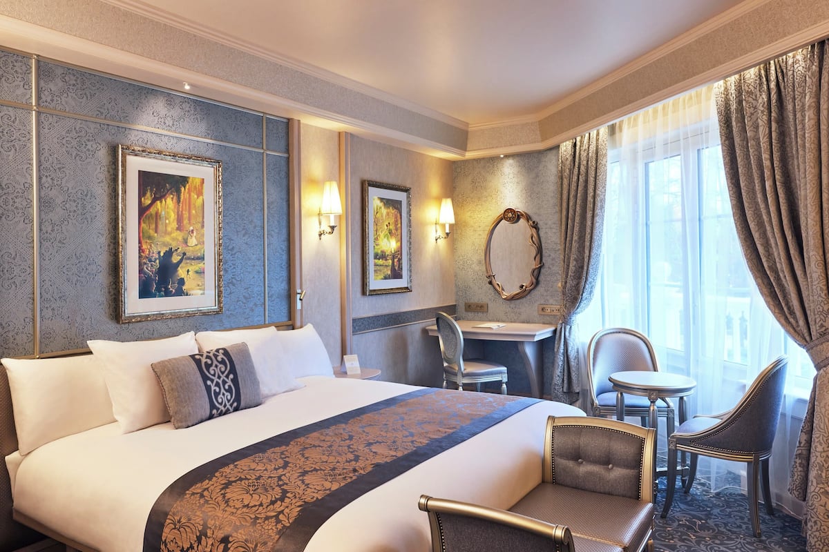 Hotellihuone, jossa on suuri sänky, työpöytä, kaksi tuolia ja näkymä ulos.