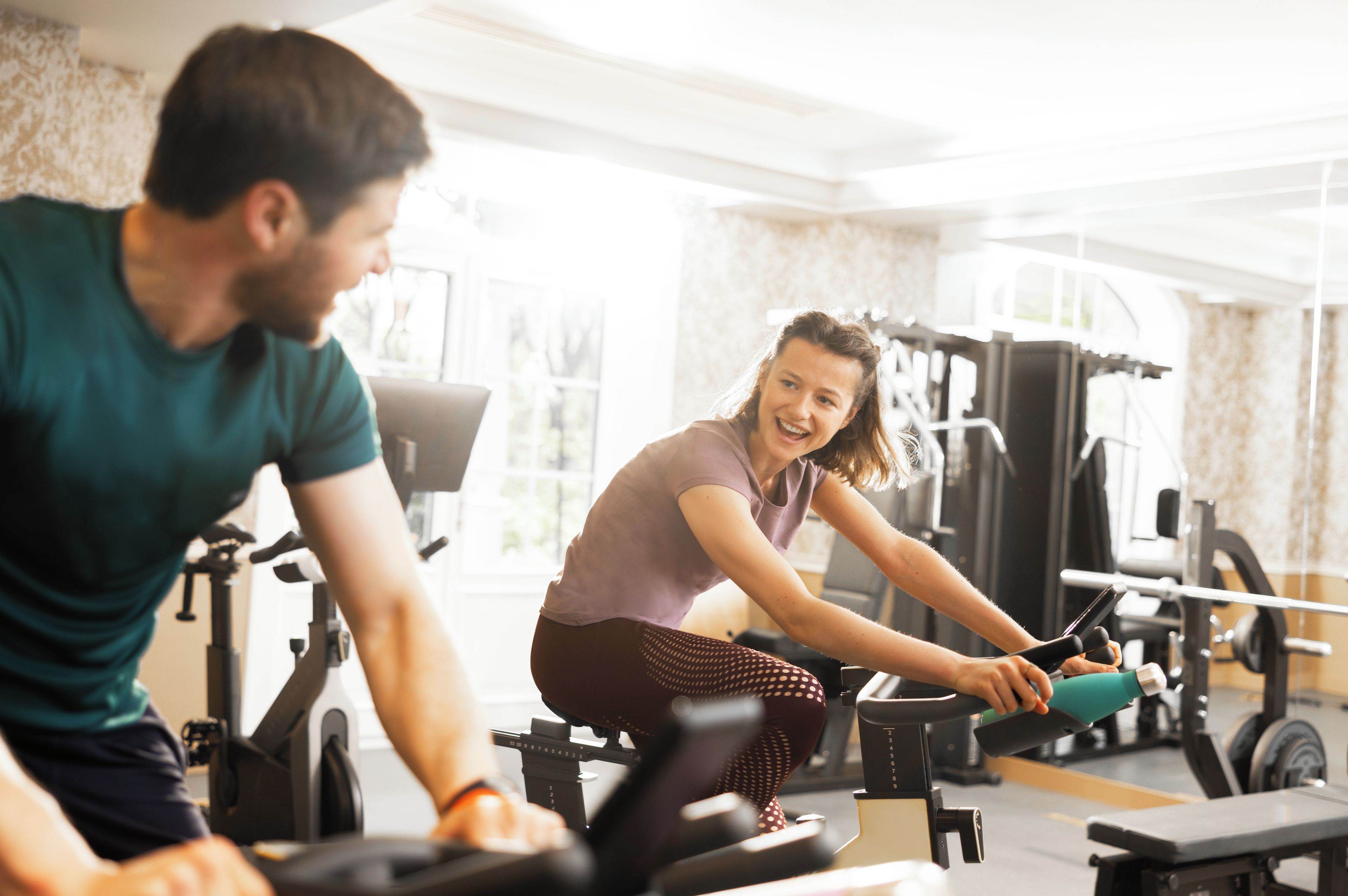 Een sportschool met trainingsapparatuur en iemand die een hometrainer gebruikt.