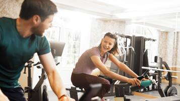 Een sportschool met trainingsapparatuur en iemand die een hometrainer gebruikt.